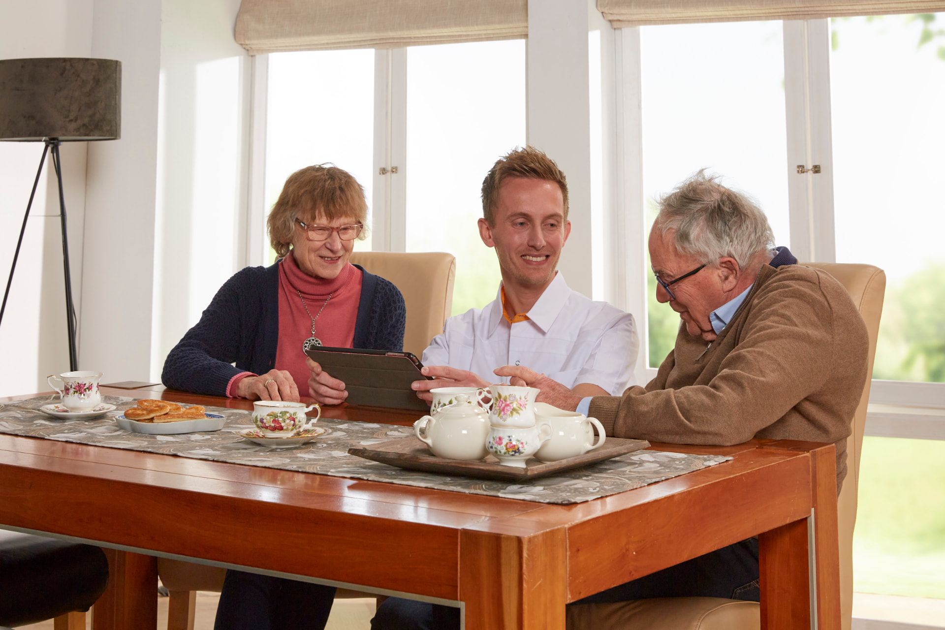 Zorgmedewerker bespreekt aan de eettafel samen met een echtpaar het leefplan op een tablet