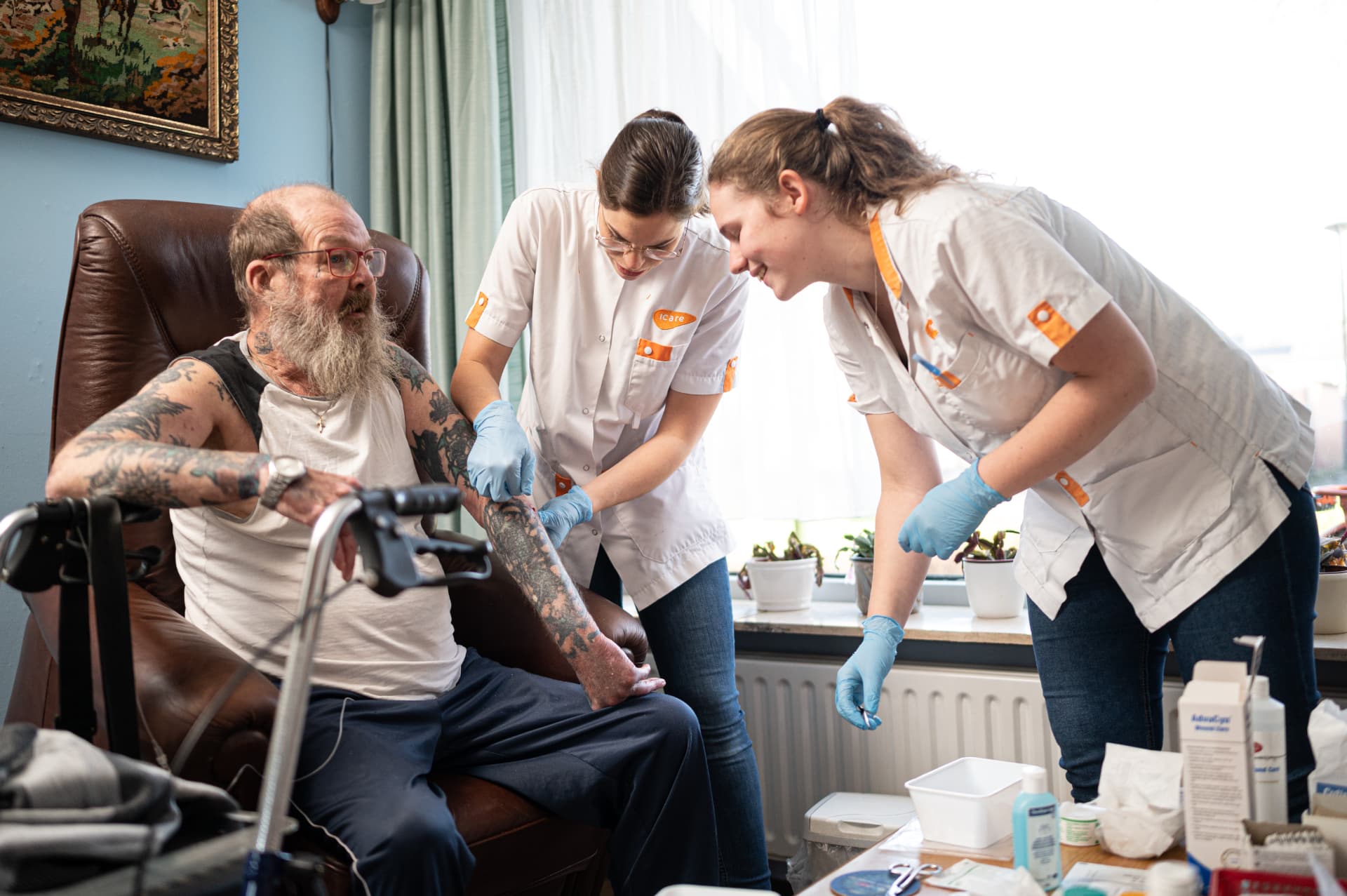 Twee verpleegkundigen verzorgen thuis het been van een man die in zijn stoel zit