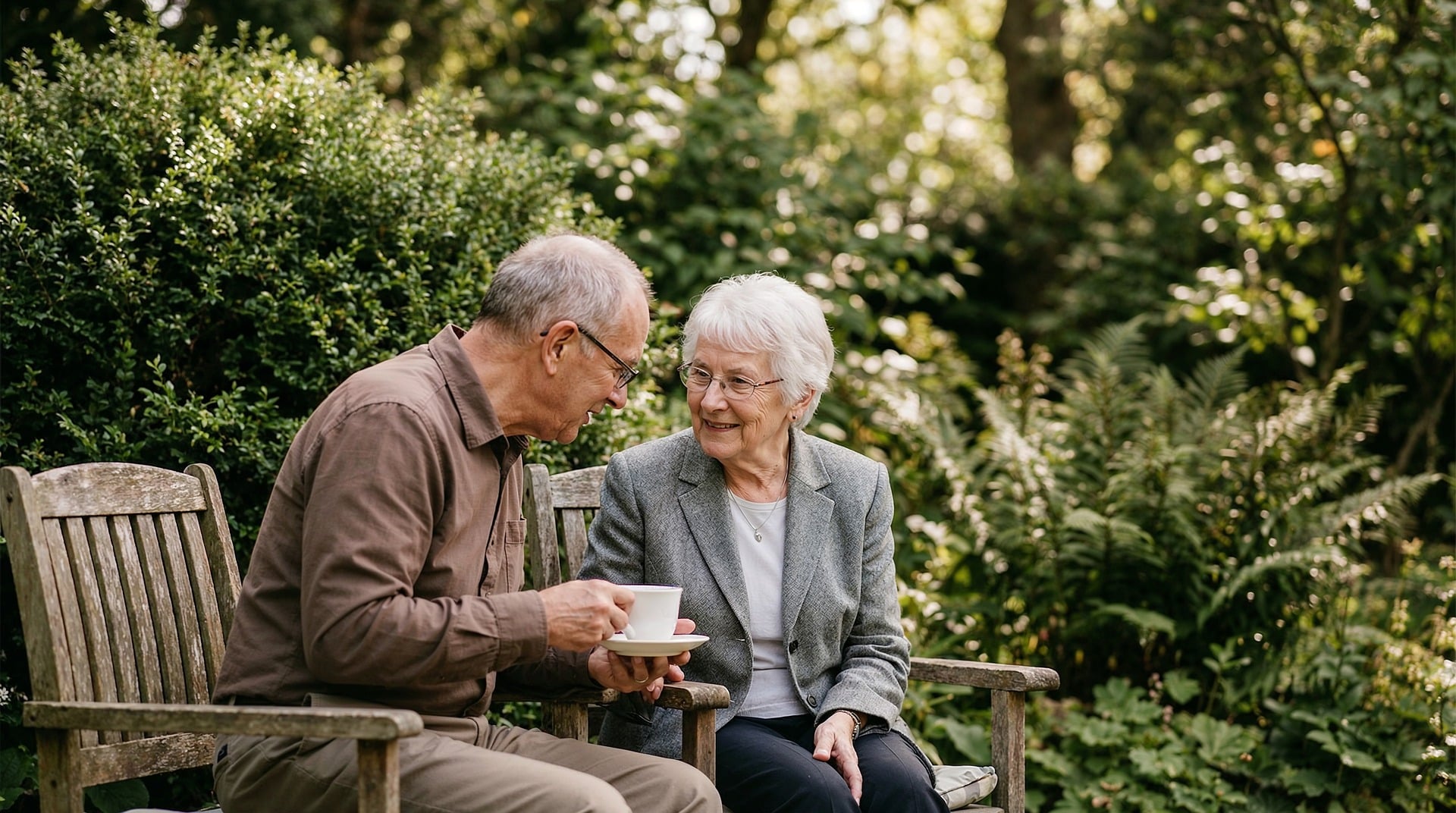 Ouder echtpaar zit met een kop koffie in de tuin en heeft een gesprek